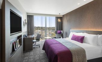 a modern hotel room with a large bed , desk , and chair , as well as a balcony offering a view of the city at Sage Melbourne Ringwood