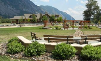 a large grassy area with a fire pit , benches , and benches , surrounded by trees and mountains in the background at Rocky Point Ranch