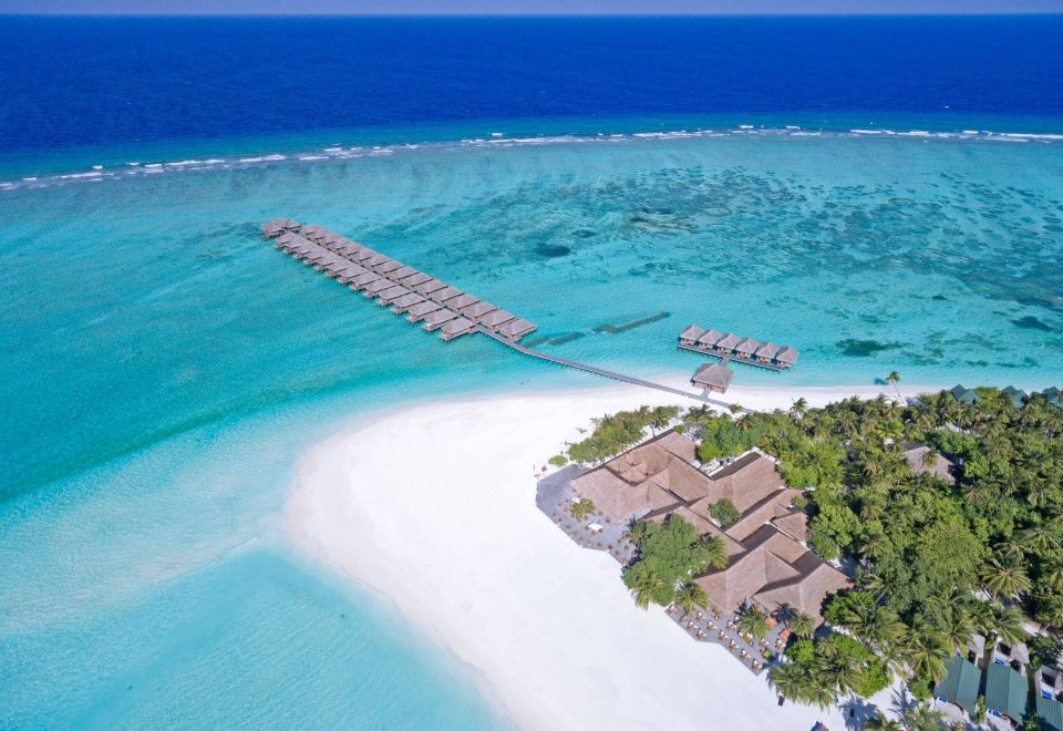 aerial view of a white sandy beach with palm trees and a group of wooden huts on stilts at Meeru Maldives Resort Island