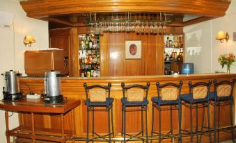 a wooden bar with a variety of chairs and bottles , as well as a coffee maker and a dining table nearby at Oxford Hotel