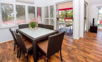 a dining room with a wooden table and chairs , surrounded by white walls and a sliding glass door leading to an outdoor patio at Ingenia Holidays South West Rocks