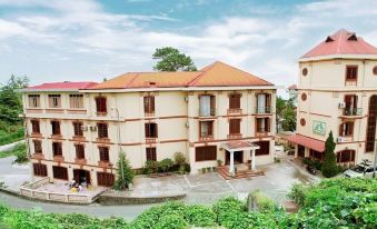 a large , beige - colored building with a red roof and balconies , surrounded by lush greenery and clear skies at Cay Thong Hotel