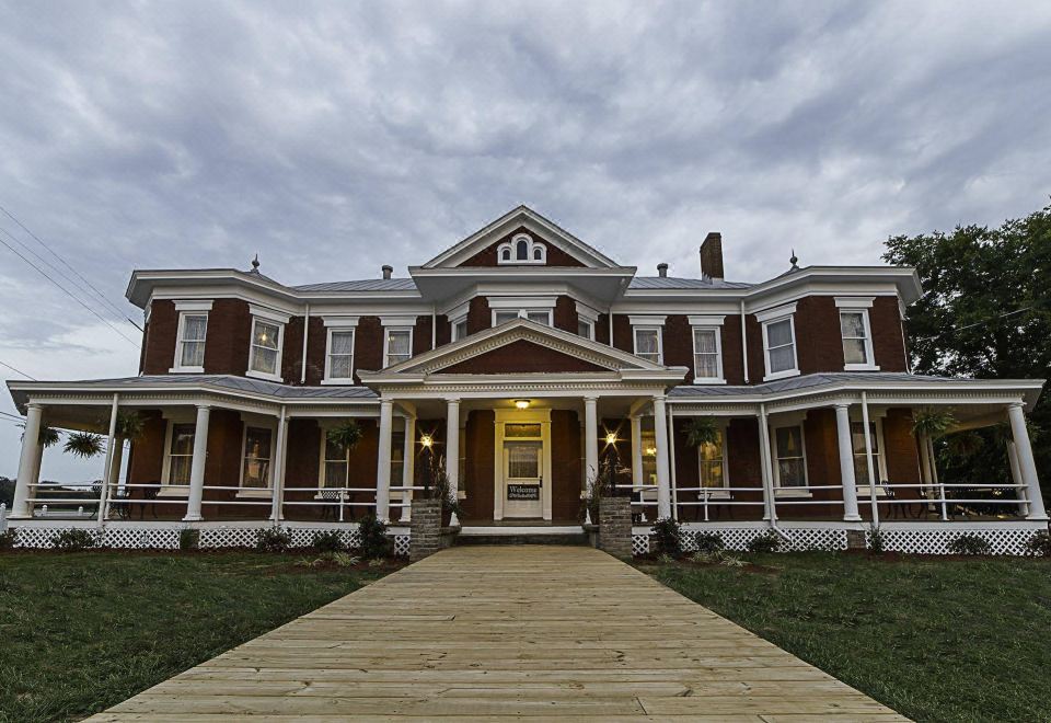 a large brown and white building with a porch and a wooden walkway leading up to it at Grand Victorian Inn