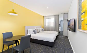 a modern hotel room with two beds , a tv , and a desk , all set against a yellow wall at ValueSuites Penrith