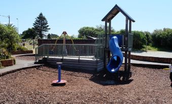 a playground with a blue slide , swing set , and other play equipment surrounded by grass at Driftwood Motel