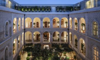 a courtyard with multiple levels of arches , surrounded by buildings and greenery , under a clear blue sky at The Jaffa, a Luxury Collection Hotel, Tel Aviv