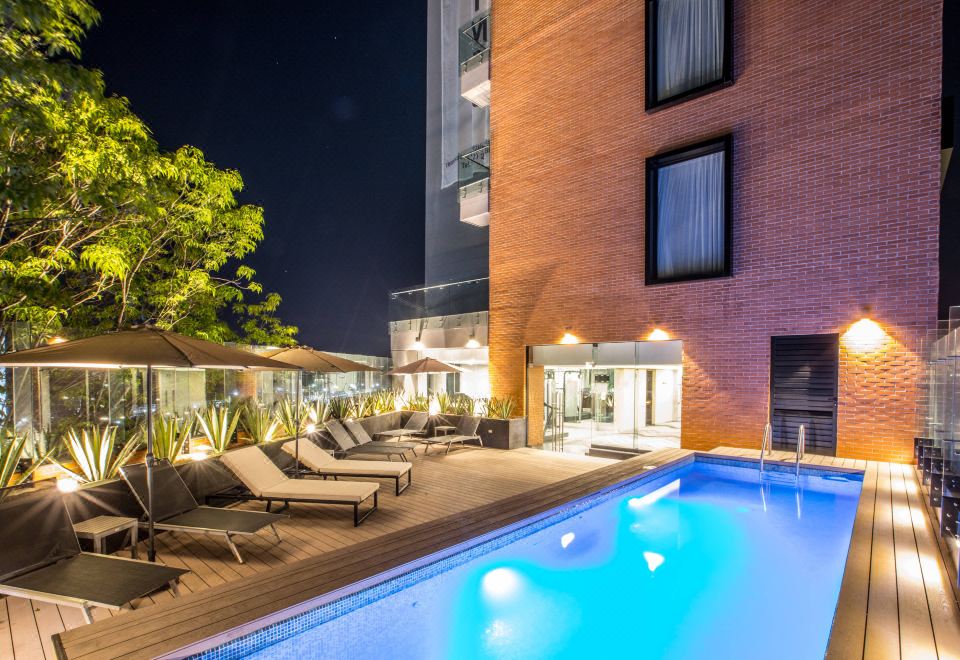 an outdoor pool surrounded by a brick building at night , with lounge chairs placed around it at Four Points by Sheraton Puebla