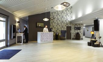 a modern hotel lobby with a reception desk , two people standing near the entrance , and geometric patterns on the walls at Novotel Manchester West