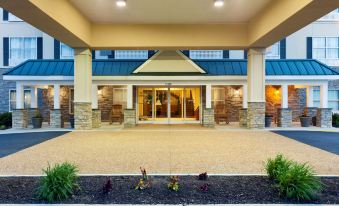 a modern hotel entrance with stone pillars , a glass door , and greenery in front of it at Country Inn & Suites by Radisson, Ashland - Hanover, VA