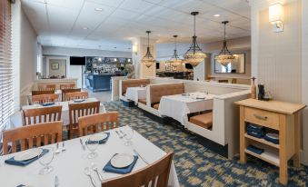 a restaurant with white tables and chairs , blue tablecloths , and pendant lights hanging from the ceiling at Holiday Inn South Kingstown (Newport Area)