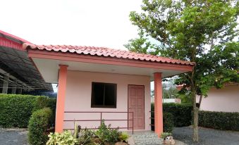 a small pink house with a red roof , surrounded by trees and bushes , situated in a grassy area at S P Resort