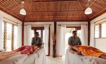 a couple of people lying on massage tables in a room with wooden ceiling and large windows at Sinalei Reef Resort & Spa