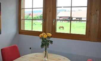 a wooden table with a vase of flowers in front of two windows , offering a view of a horse - drawn carriage at Simcha