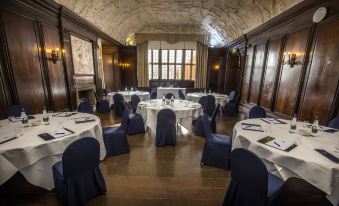 a large , empty banquet hall with multiple round tables set for a formal event , all covered in white tablecloths and blue chairs at Portmeirion Village & Castell Deudraeth