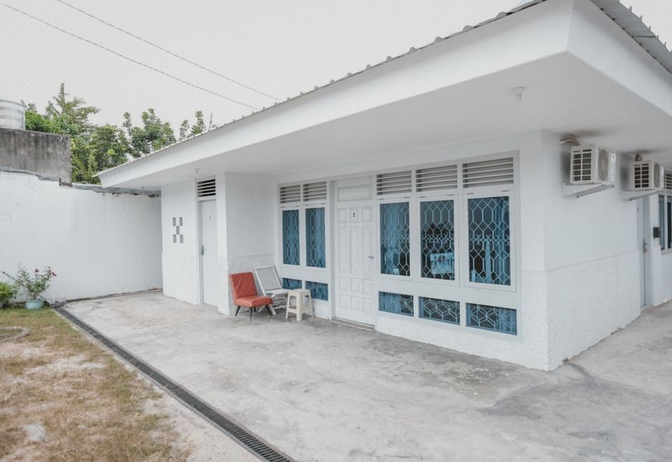 a white house with blue windows and doors , surrounded by a concrete driveway and a red chair at RedDoorz @ Beringin Jambi