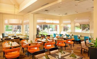 a restaurant with multiple tables and chairs , each table has a white tablecloth and green napkins at Hilton Garden Inn Philadelphia/Ft. Washington