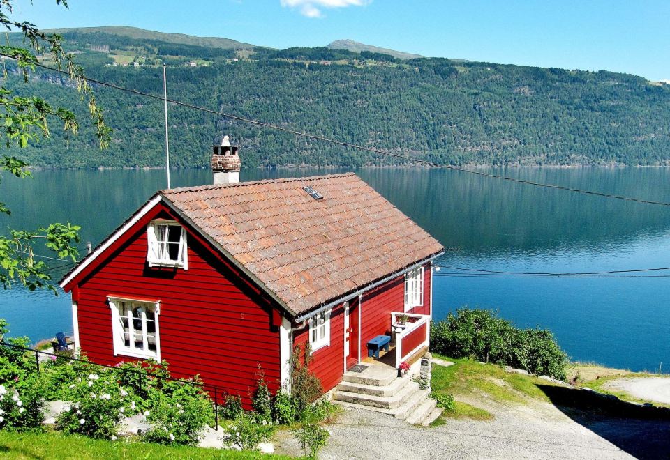 a red house situated on a hillside , overlooking a body of water in the background at Juv