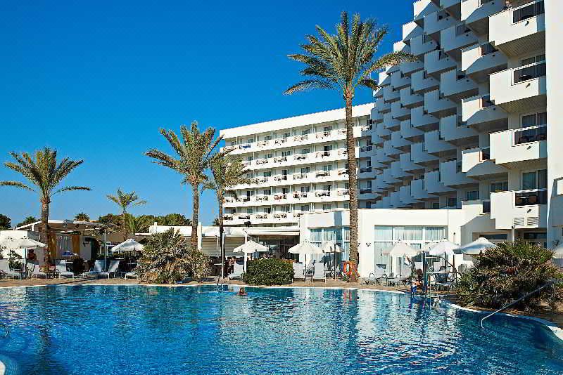 a large white hotel with a swimming pool in front of it , surrounded by palm trees at Hipotels Flamenco