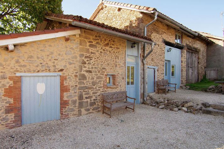 a stone building with blue doors and a bench in front of it , situated on a gravel path at La Tulipe