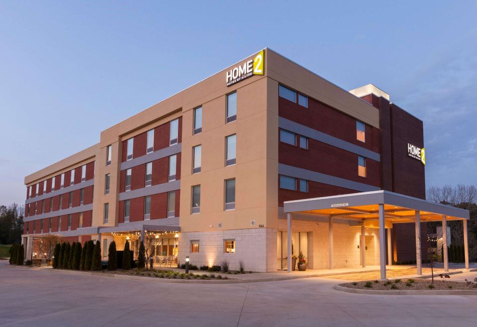 "a large hotel with a yellow "" home 2 "" sign on the front and a covered parking lot in front" at Home2 Suites by Hilton Canton