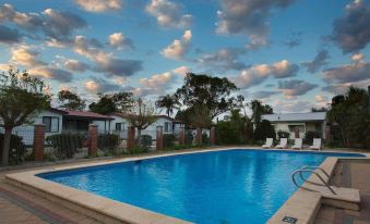 a large swimming pool is surrounded by white chairs and trees , with a house in the background at Discovery Parks - Perth Airport