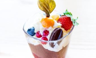 a cup filled with chocolate pudding , topped with whipped cream , berries , and a garnish , sitting on a wooden table at Fosshotel Eastfjords