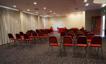 a large conference room with rows of red chairs and white walls , ready for an event at Ambassador Hotel