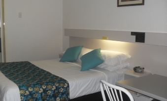 a bed with a blue and white quilt is in a room next to a white chair at Balonne River Motor Inn