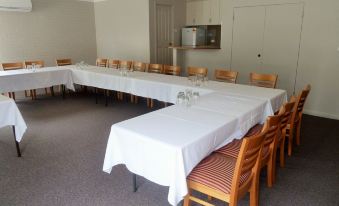 a large dining table with white tablecloths and chairs in a room with beige walls at The Aston Motel Tamworth