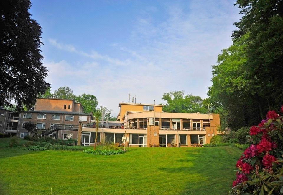 a large brick building surrounded by a lush green lawn , with trees in the background at Fletcher Parkhotel Val Monte