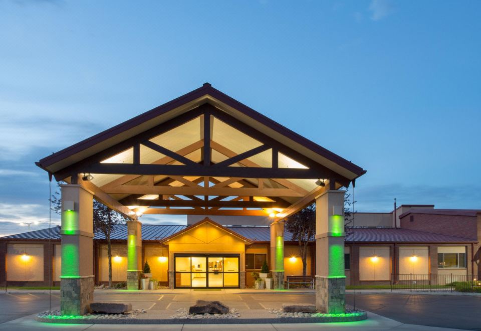 a large building with a wooden roof and a covered entrance , lit up at night at Holiday Inn Riverton-Convention Center