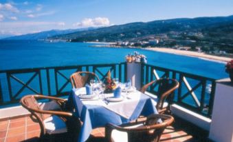 a table set with a blue tablecloth , wine glasses , and utensils on a balcony overlooking the ocean at Erofili Beach Hotel