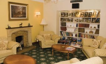a cozy living room with a fireplace , two couches , and a bookshelf filled with books at Glenspean Lodge Hotel
