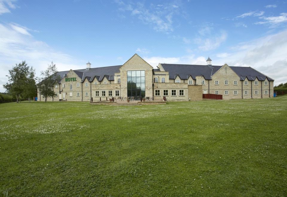 a large , modern building with a green lawn and a clear blue sky in the background at Best Western Plus Pastures Hotel