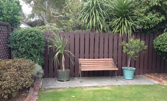 a wooden bench is placed in a garden with two potted plants and a fence at Asure Green Gables Motel