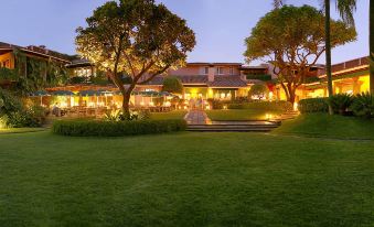 a large , well - maintained lawn with trees and a building in the background , lit up at night at Las Mañanitas