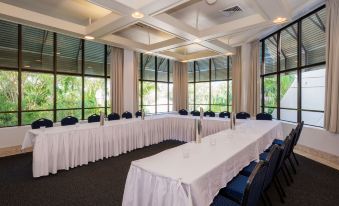 a large conference room with multiple long tables and white tablecloths , surrounded by chairs , in front of a window at Greenmount Beach House