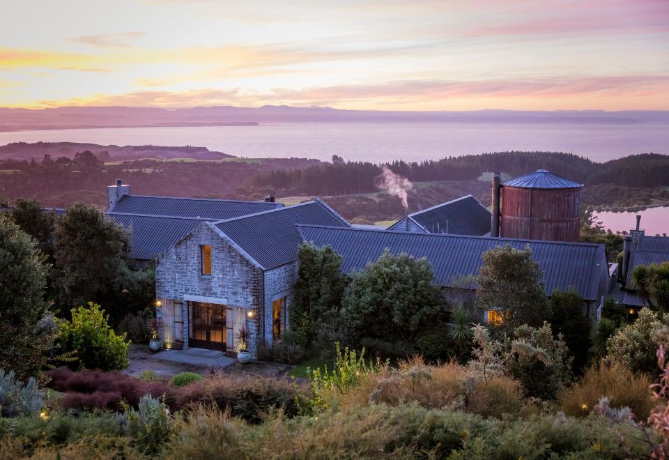 a large stone house with a red roof , surrounded by trees and overlooking a body of water at Rosewood Cape Kidnappers