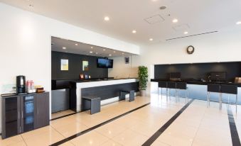 a modern hotel lobby with a check - in desk and a television mounted on the wall at Dormy Inn Mishima