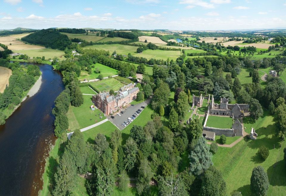 aerial view of a large , old castle surrounded by green fields and trees , with a river flowing nearby at Dryburgh Abbey Hotel