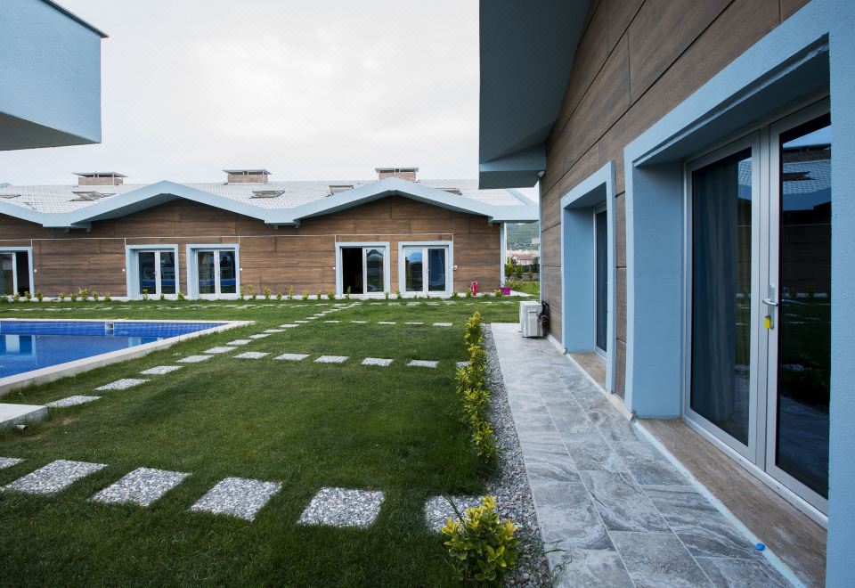 a modern house with a green lawn , stone pathway , and blue shutters is surrounded by a large concrete block wall at La Vida Hotel