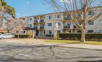 a multi - story apartment building surrounded by trees and grass , with a car parked in front of it at Canning Bridge Auto Lodge