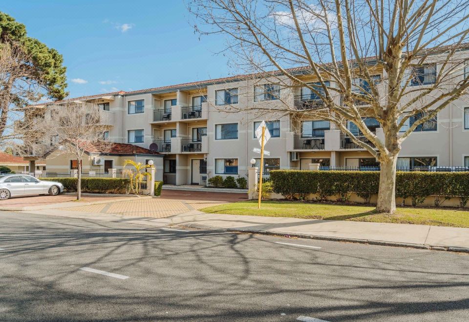 a multi - story apartment building surrounded by trees and grass , with a car parked in front of it at Canning Bridge Auto Lodge