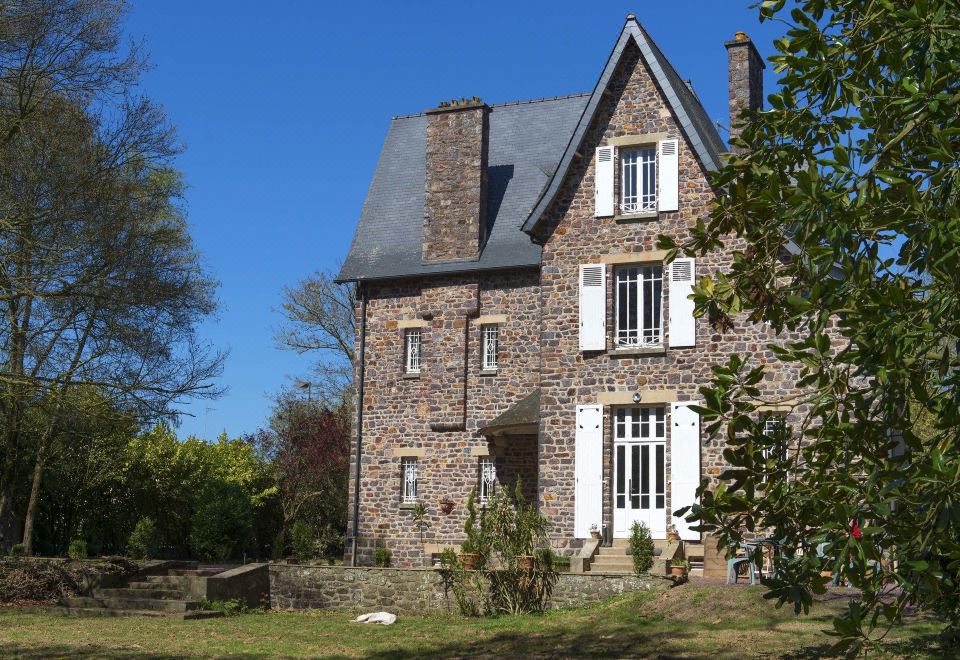a large stone house with a gray roof and white windows is surrounded by trees at La Maison Rouge Broceliande