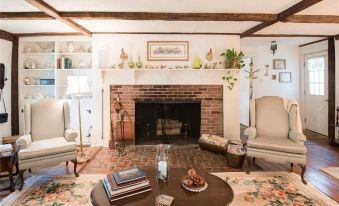 a cozy living room with a brick fireplace , two chairs , a coffee table , and various books at The Bond 1835