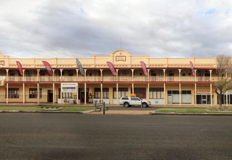 a large beige building with red flags flying , surrounded by cars parked on the street and cars driving past at Hotel Corones