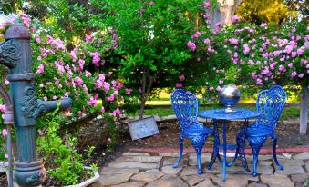 a blue table and chair are set up in a garden with pink flowers , creating a picturesque setting at Southern Rose Ranch