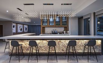 a modern bar area with a marble counter , black stools , and a chandelier hanging from the ceiling at AC Hotel San Jose Escazu