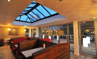 a modern restaurant with wooden tables and chairs , a large skylight , and a glass door at Best Western Plus Oaklands Hotel