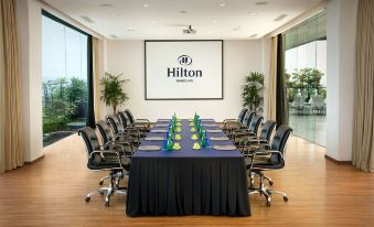 a conference room with a large table surrounded by chairs , and a projector screen displaying the hilton logo at Hilton Bandung